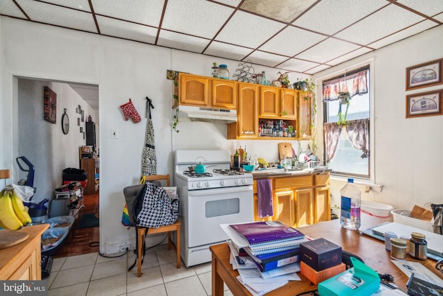 kitchen with a drop ceiling, white gas range, and light tile patterned floors