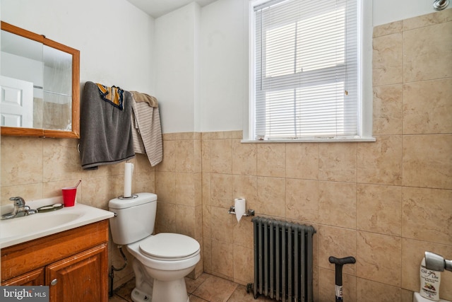 bathroom with radiator, vanity, toilet, tile walls, and tile patterned flooring