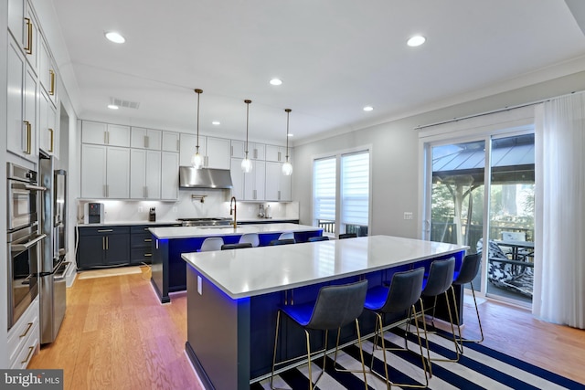 kitchen with white cabinetry, hanging light fixtures, an island with sink, a kitchen bar, and light wood-type flooring