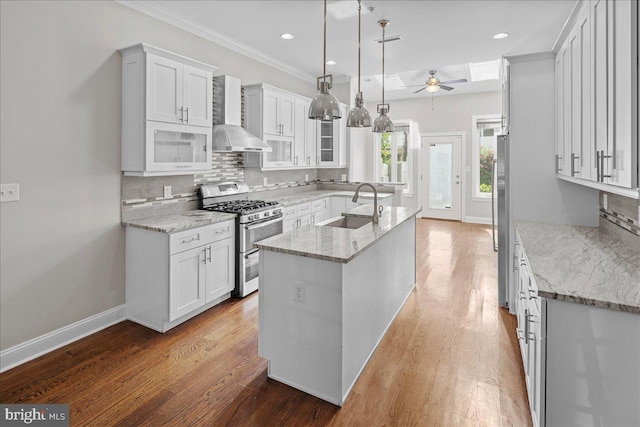 kitchen with white cabinets, wall chimney exhaust hood, sink, appliances with stainless steel finishes, and decorative light fixtures