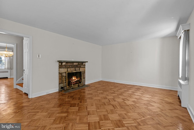 unfurnished living room with an inviting chandelier, radiator, light parquet floors, and a stone fireplace