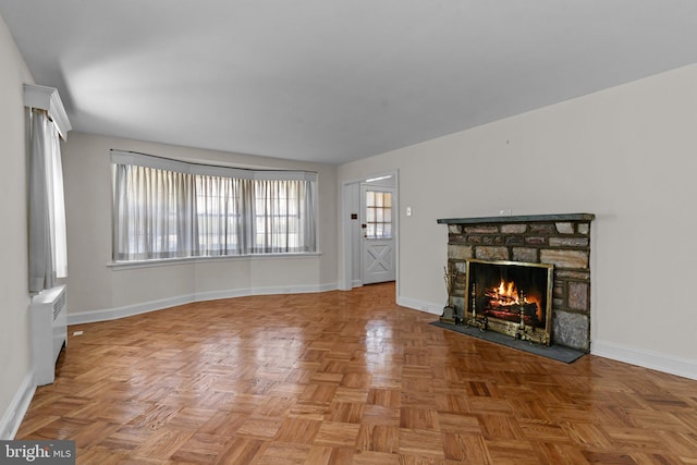 unfurnished living room with a stone fireplace, light parquet flooring, and radiator