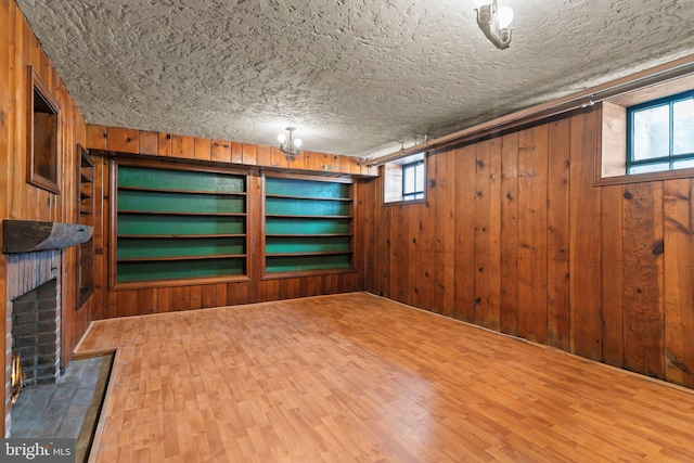 basement with wood-type flooring, a brick fireplace, wooden walls, and a textured ceiling