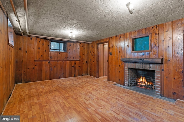 basement with wood-type flooring, a textured ceiling, wooden walls, and a brick fireplace