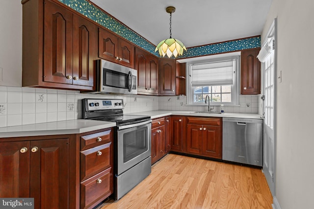 kitchen featuring tasteful backsplash, light hardwood / wood-style flooring, decorative light fixtures, sink, and appliances with stainless steel finishes