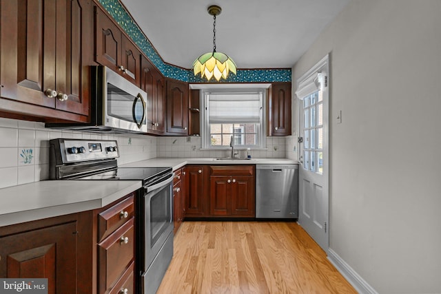 kitchen with decorative backsplash, sink, light hardwood / wood-style floors, hanging light fixtures, and appliances with stainless steel finishes