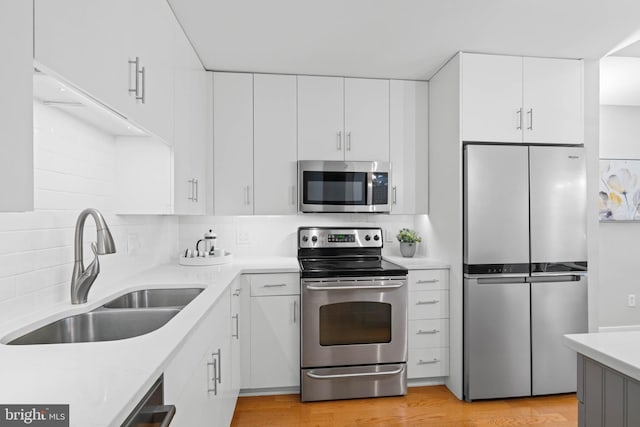 kitchen with appliances with stainless steel finishes, light wood-type flooring, white cabinetry, and sink