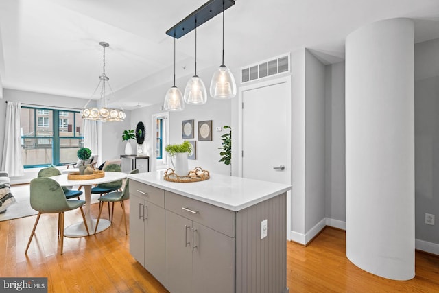 kitchen with gray cabinets, decorative light fixtures, a kitchen island, and light hardwood / wood-style floors