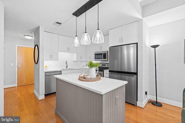 kitchen featuring a kitchen island, appliances with stainless steel finishes, decorative light fixtures, light hardwood / wood-style floors, and white cabinetry