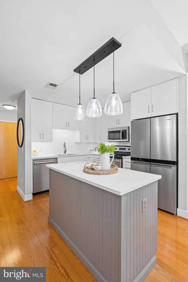 kitchen featuring white cabinetry, a center island, stainless steel appliances, light hardwood / wood-style flooring, and pendant lighting