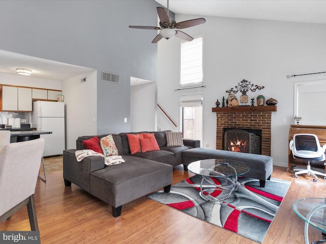 living room featuring a brick fireplace, high vaulted ceiling, light hardwood / wood-style flooring, and ceiling fan