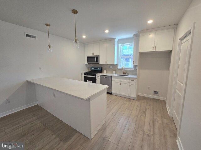 kitchen featuring stainless steel appliances, backsplash, decorative light fixtures, light hardwood / wood-style floors, and white cabinets