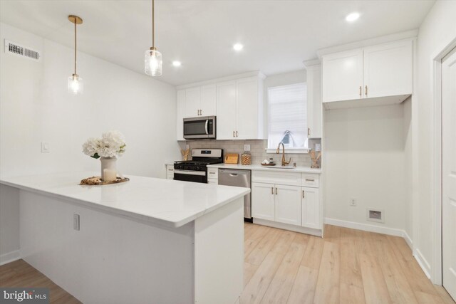 kitchen with stainless steel appliances, hanging light fixtures, sink, white cabinetry, and light wood-type flooring