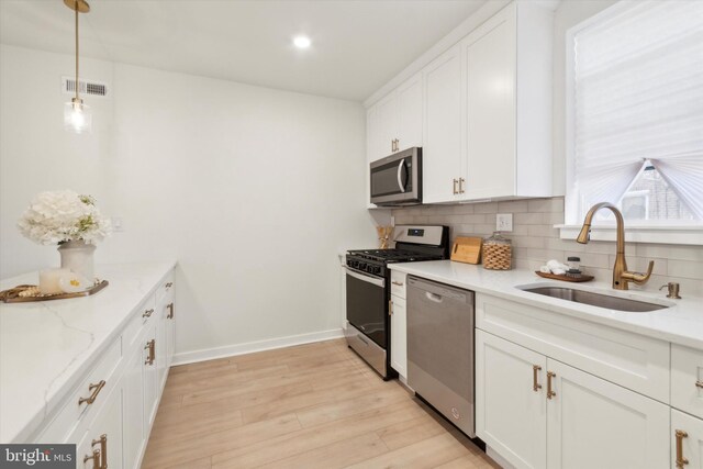 kitchen with light hardwood / wood-style flooring, sink, white cabinetry, appliances with stainless steel finishes, and decorative light fixtures