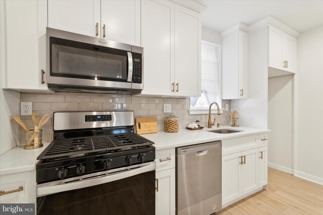 kitchen with light stone counters, light hardwood / wood-style flooring, sink, white cabinetry, and appliances with stainless steel finishes