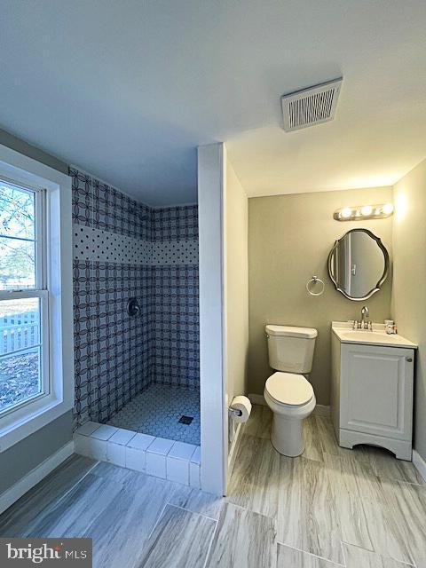 bathroom with a tile shower, vanity, and toilet