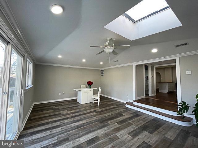 interior space with dark hardwood / wood-style floors, ceiling fan, crown molding, and a skylight