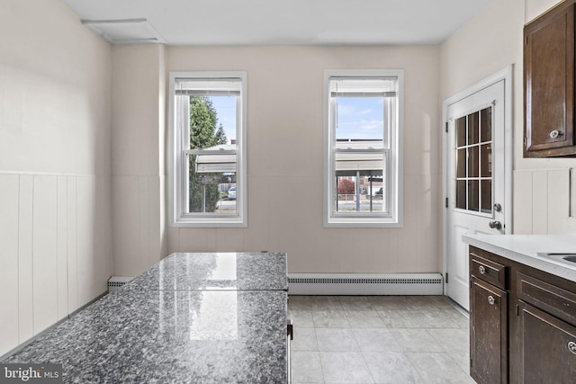 kitchen featuring a baseboard radiator, dark brown cabinets, dark stone counters, and light tile patterned flooring