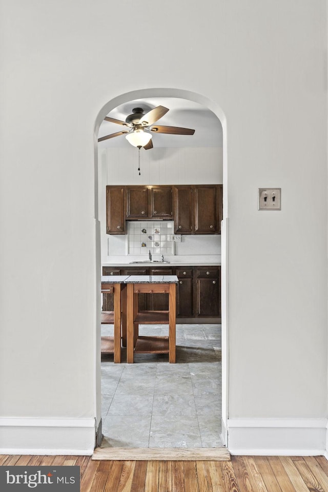 bar with light wood-type flooring, sink, dark brown cabinets, ceiling fan, and decorative backsplash