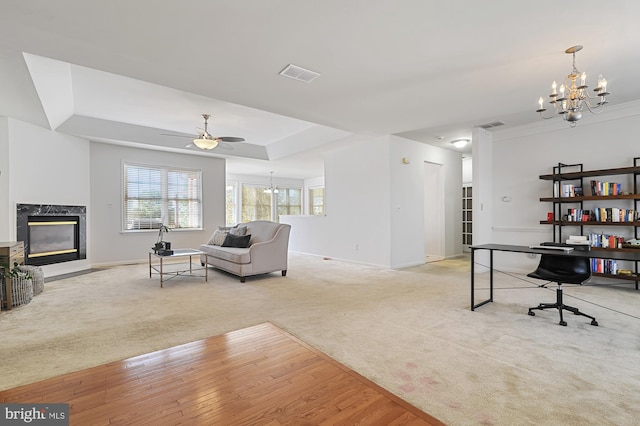 carpeted living room featuring ceiling fan with notable chandelier, a high end fireplace, and a tray ceiling