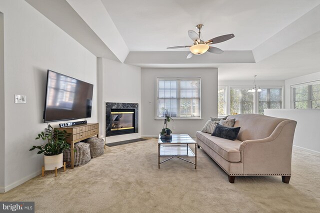 carpeted living room with ceiling fan with notable chandelier, a high end fireplace, and a raised ceiling