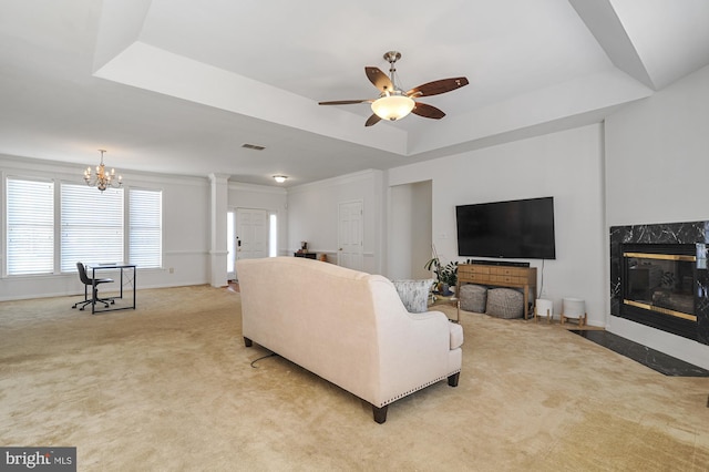 living room featuring ornate columns, light carpet, a raised ceiling, a fireplace, and ceiling fan with notable chandelier