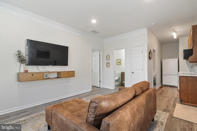 living room featuring washer / clothes dryer, sink, ornamental molding, and light wood-type flooring