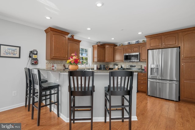 kitchen with light hardwood / wood-style floors, appliances with stainless steel finishes, kitchen peninsula, and a kitchen breakfast bar