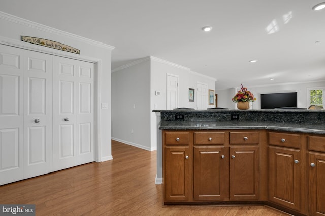 kitchen featuring ornamental molding, light wood-type flooring, and dark stone countertops