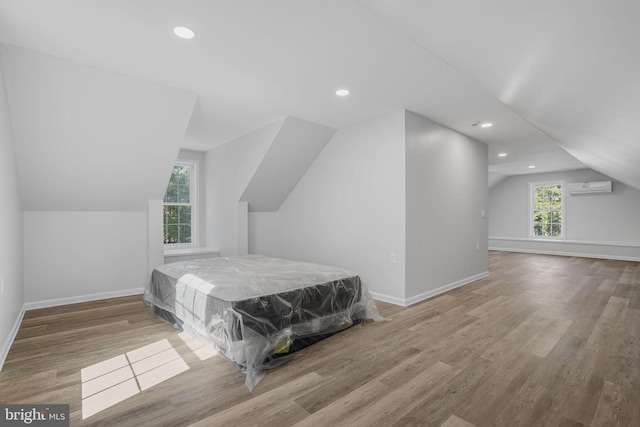 bedroom featuring a wall mounted air conditioner, light hardwood / wood-style flooring, and vaulted ceiling