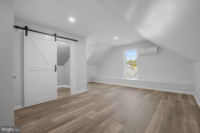 additional living space featuring light wood-type flooring, a barn door, lofted ceiling, and a wall unit AC