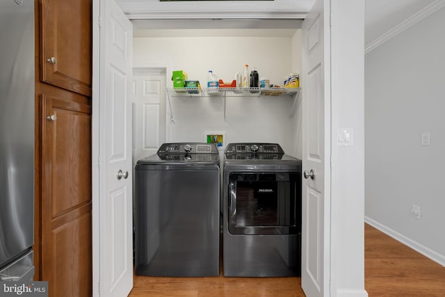 laundry area with light wood-type flooring, crown molding, and washer and dryer