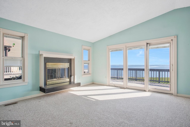 unfurnished living room with lofted ceiling, a textured ceiling, a water view, and carpet flooring