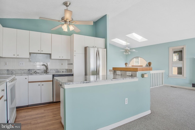 kitchen with appliances with stainless steel finishes, vaulted ceiling with skylight, and white cabinetry