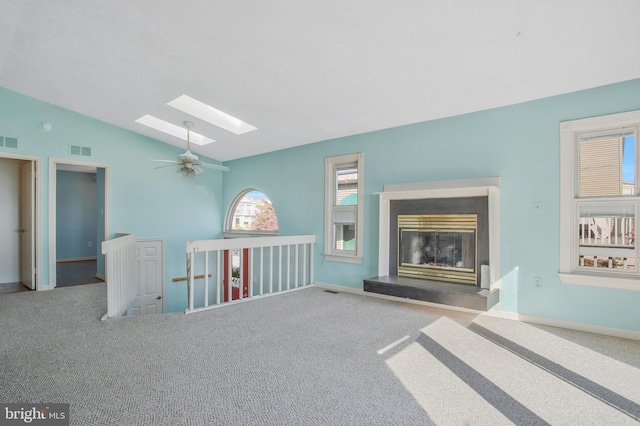 unfurnished living room with vaulted ceiling with skylight, carpet flooring, and ceiling fan