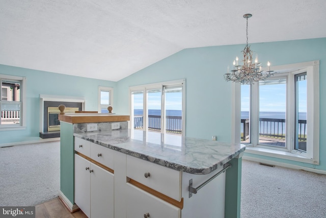 kitchen featuring white cabinetry, a water view, hanging light fixtures, and a healthy amount of sunlight