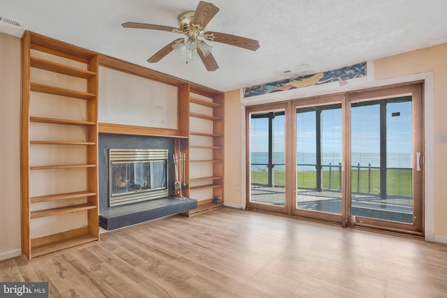 unfurnished living room with light hardwood / wood-style floors, a textured ceiling, and a water view