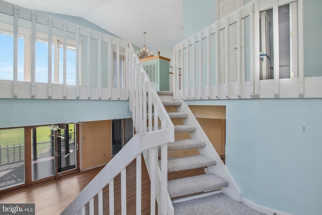 stairs with a chandelier, vaulted ceiling, hardwood / wood-style flooring, and a healthy amount of sunlight