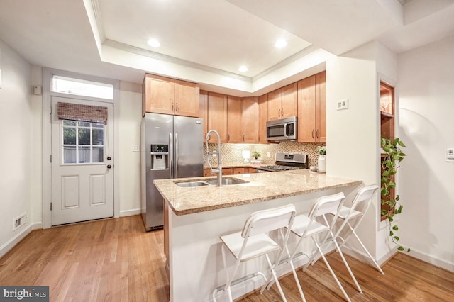 kitchen featuring stainless steel appliances, light wood-type flooring, kitchen peninsula, backsplash, and a tray ceiling