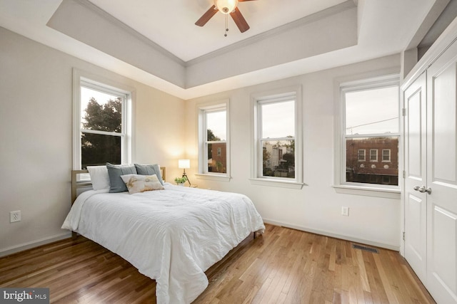 bedroom with ceiling fan, light hardwood / wood-style flooring, crown molding, and a tray ceiling