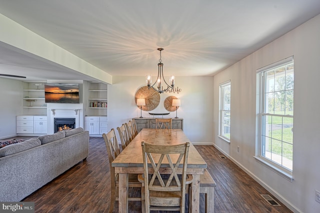 dining area with built in shelves, dark hardwood / wood-style floors, an inviting chandelier, and plenty of natural light