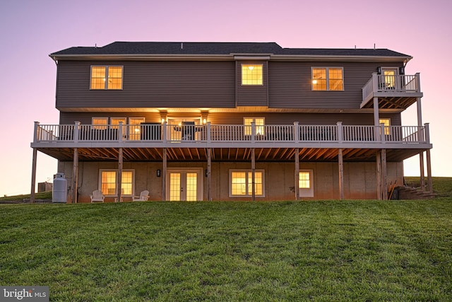 back house at dusk featuring a lawn and a balcony