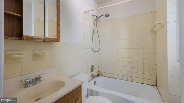 full bathroom with vanity, toilet, tiled shower / bath, and tile walls