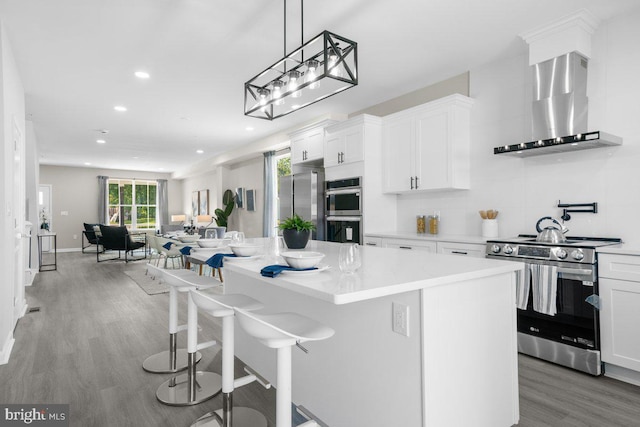 kitchen featuring a kitchen island, a breakfast bar area, white cabinetry, wall chimney exhaust hood, and stainless steel appliances