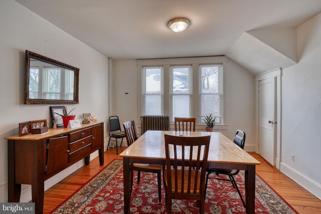 dining space with baseboards, light wood finished floors, and vaulted ceiling