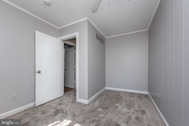 unfurnished bedroom featuring light colored carpet, ceiling fan, crown molding, and wood walls