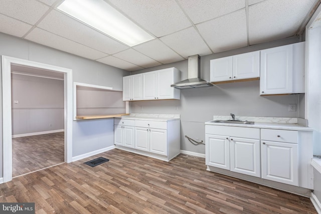 kitchen featuring sink, wall chimney range hood, dark hardwood / wood-style floors, a paneled ceiling, and white cabinets