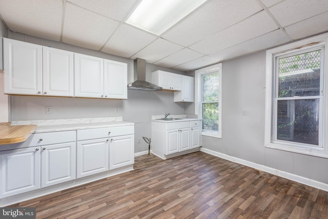 kitchen with a paneled ceiling, wall chimney exhaust hood, white cabinets, and dark wood-type flooring