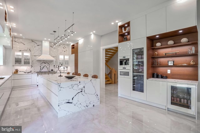 kitchen featuring light stone countertops, hanging light fixtures, white cabinetry, a large island, and custom range hood