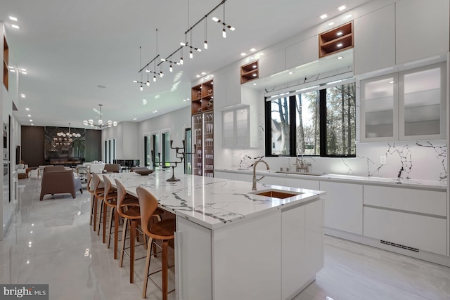 kitchen with a large island with sink, decorative backsplash, sink, a notable chandelier, and white cabinetry